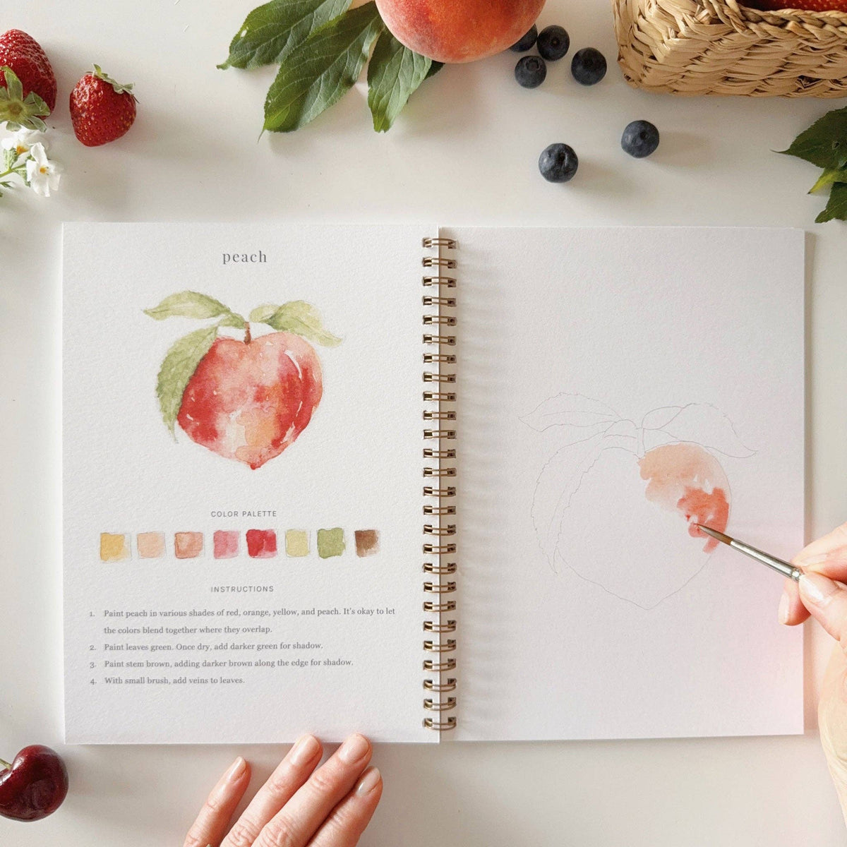 Botanical fruit watercolor workbook displayed with seasonal fruit, art supplies, and natural textures, inspiring a relaxing afternoon of creativity.