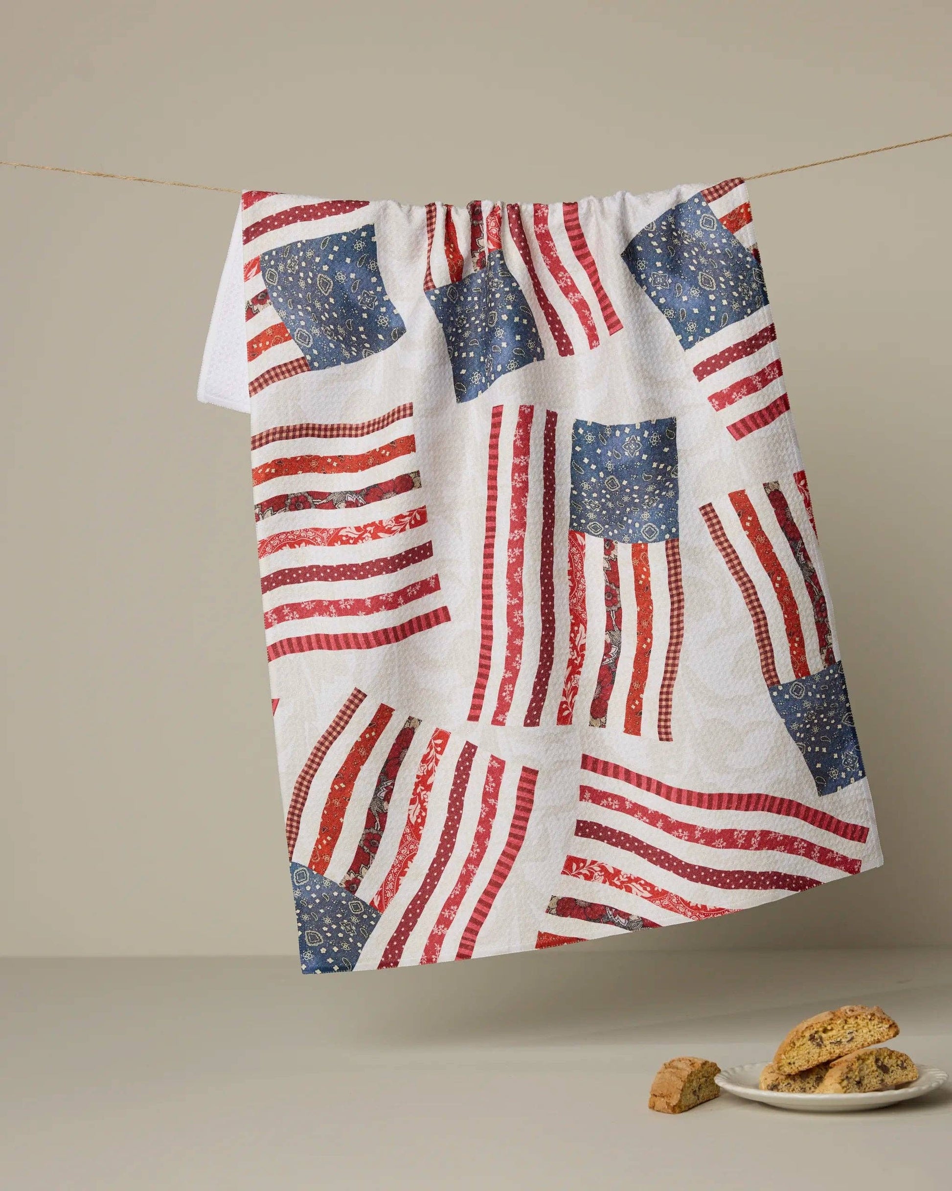 Tea towel with American flag pattern hanging on a line, with cookies on a plate below.