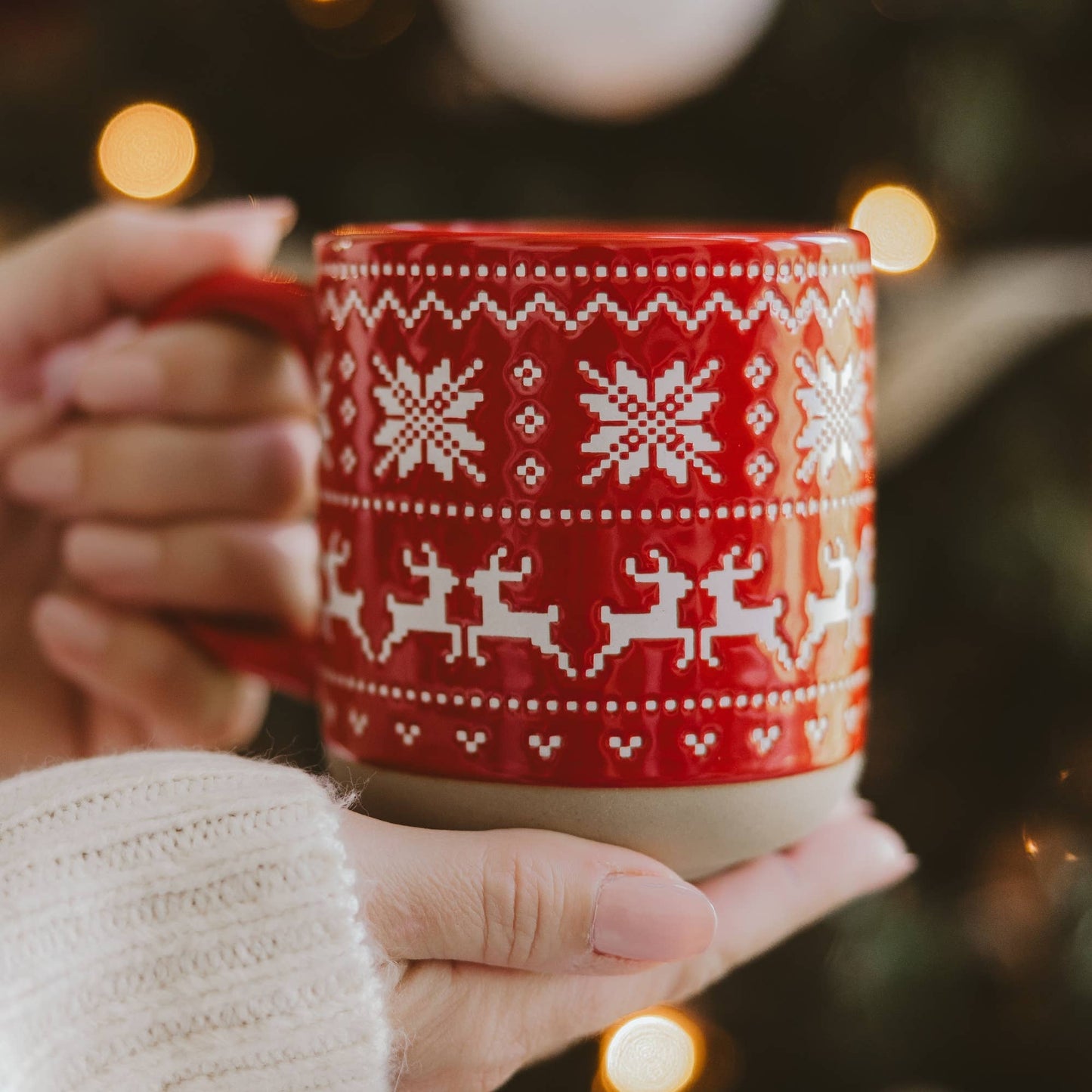 Red stoneware coffee mug featuring an embossed Fair Isle pattern with woodland deer and snowflakes, finished with a speckled glaze and exposed natural stoneware base.