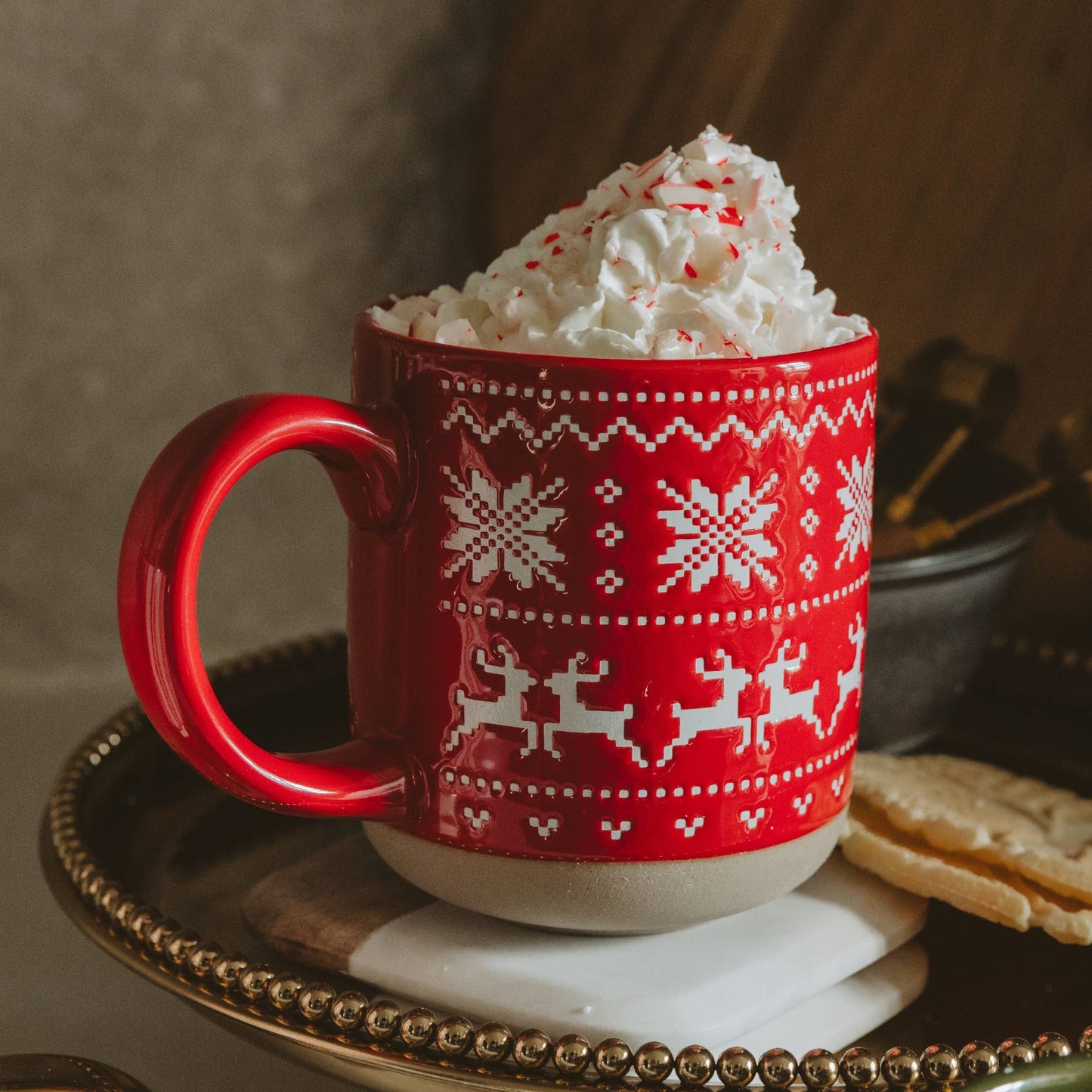 Red Fair Isle stoneware coffee mug filled with hot cocoa and styled with evergreen branches, pinecones, and cozy knit textiles.
