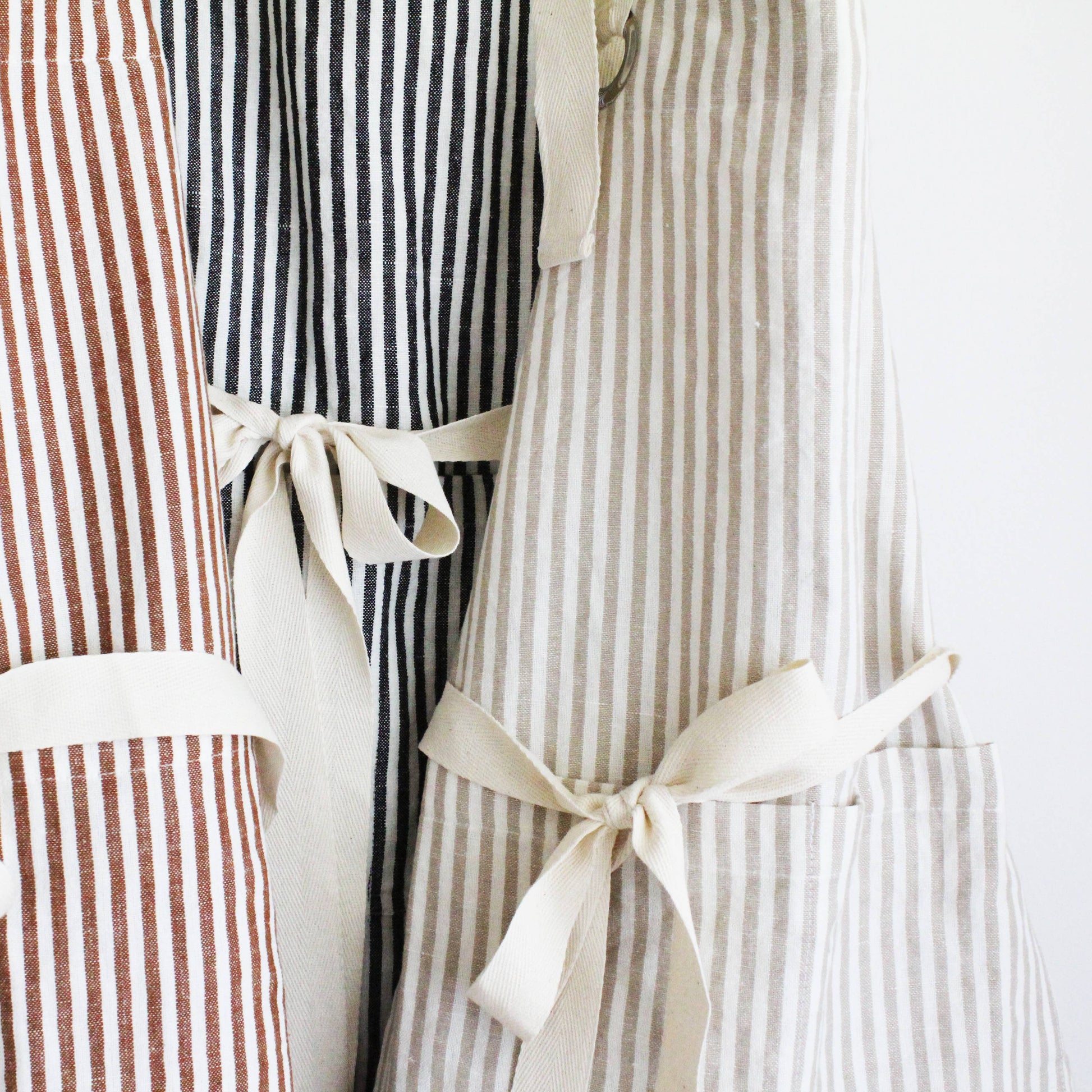 Close-up of the Rust Pinstripe Ruffle Apron showcasing the classic pinstripe fabric, feminine ruffle trim, and functional front pocket.