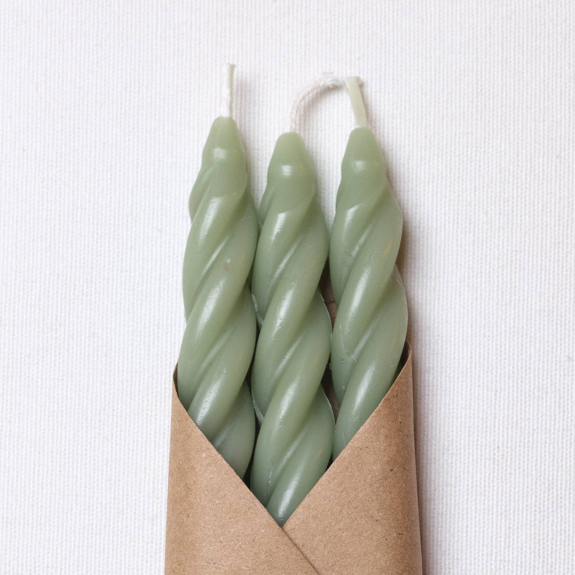 Set of three handcrafted spiral beeswax taper candles in a soft sage green color.