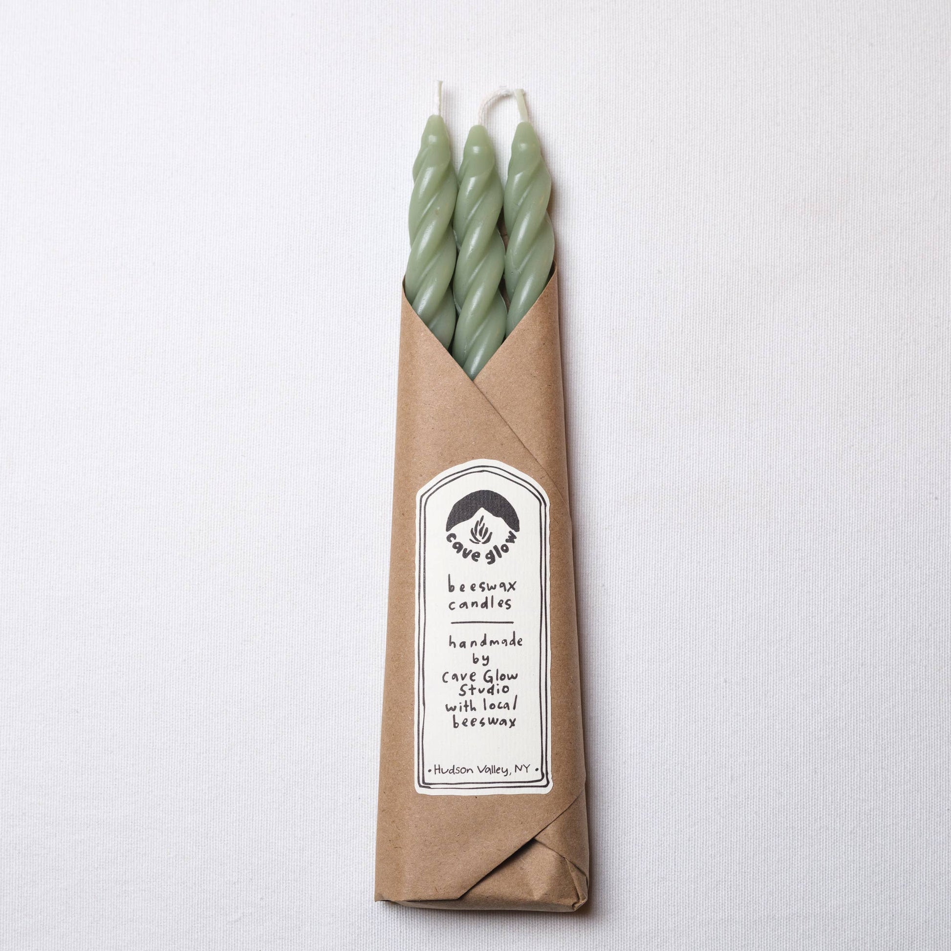Set of three handcrafted spiral beeswax taper candles in a soft sage green color.