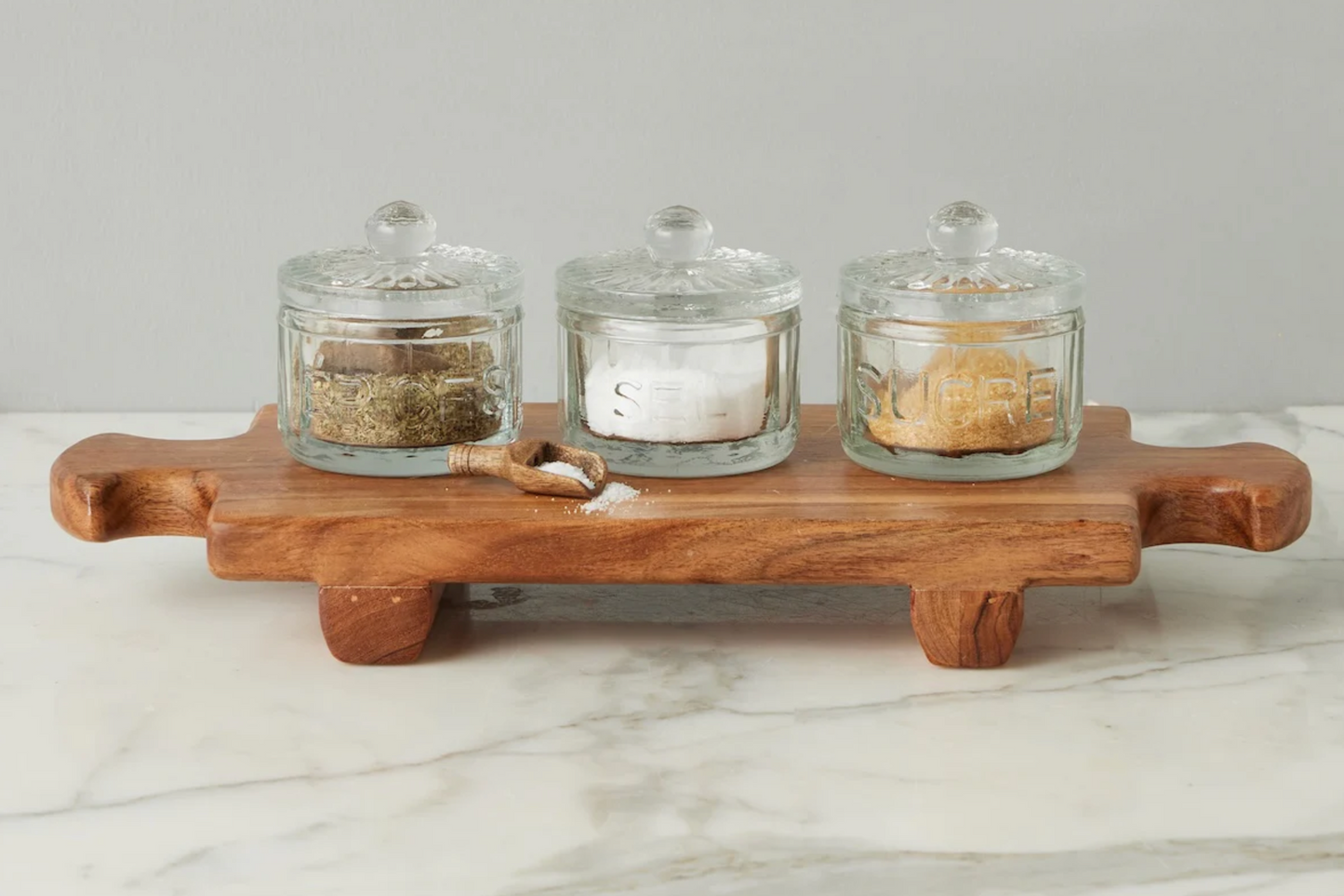 Wooden tray with three glass jars on a marble surface