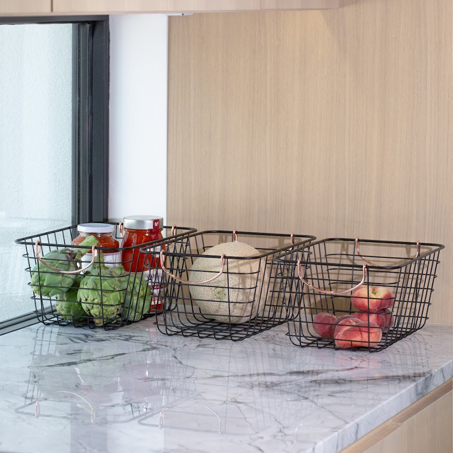 Three black wire baskets on a marble countertop with various items inside.