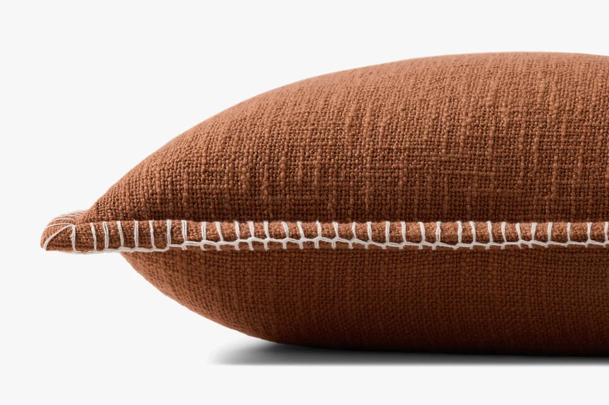 Close-up of the terracotta woven pillow highlighting the textured cotton fabric, white contrast stitching, flange edge, and hidden zipper with antique bronze Loloi logo pull.