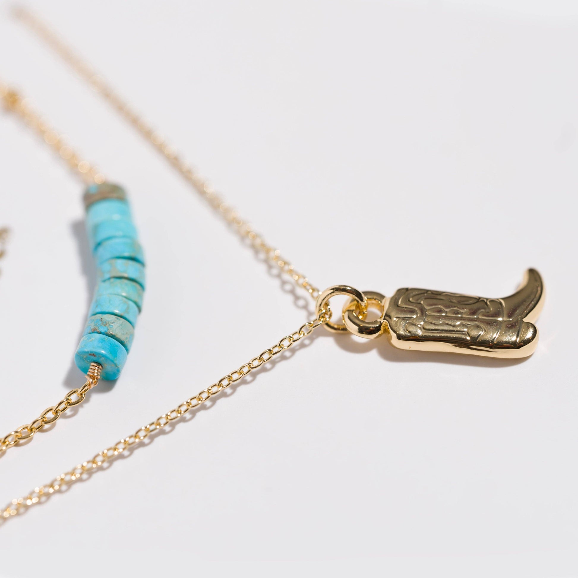 Close-up of natural turquoise bead necklace layered with an 18k gold-coated cowboy boot charm necklace.