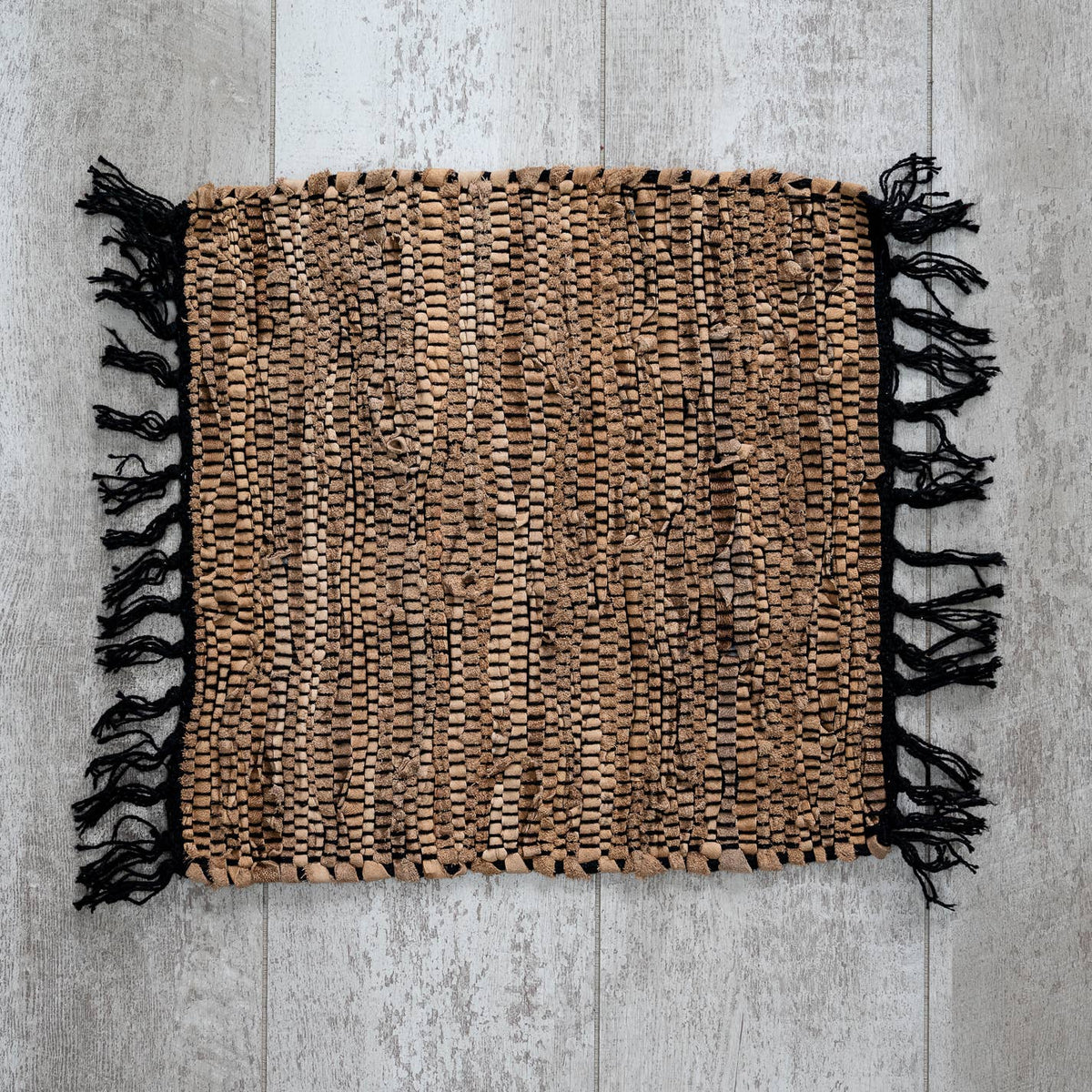 Light tan woven leather placemat with fringe detailing, measuring 20 by 15 inches.