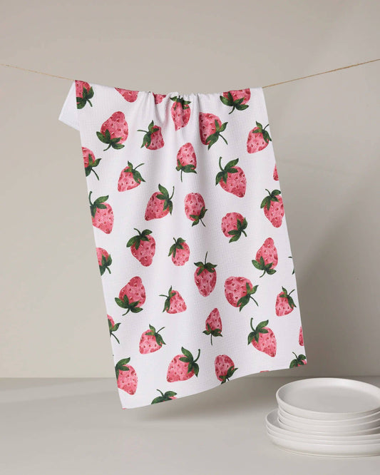 Towel with strawberry pattern hanging on a line against a neutral background