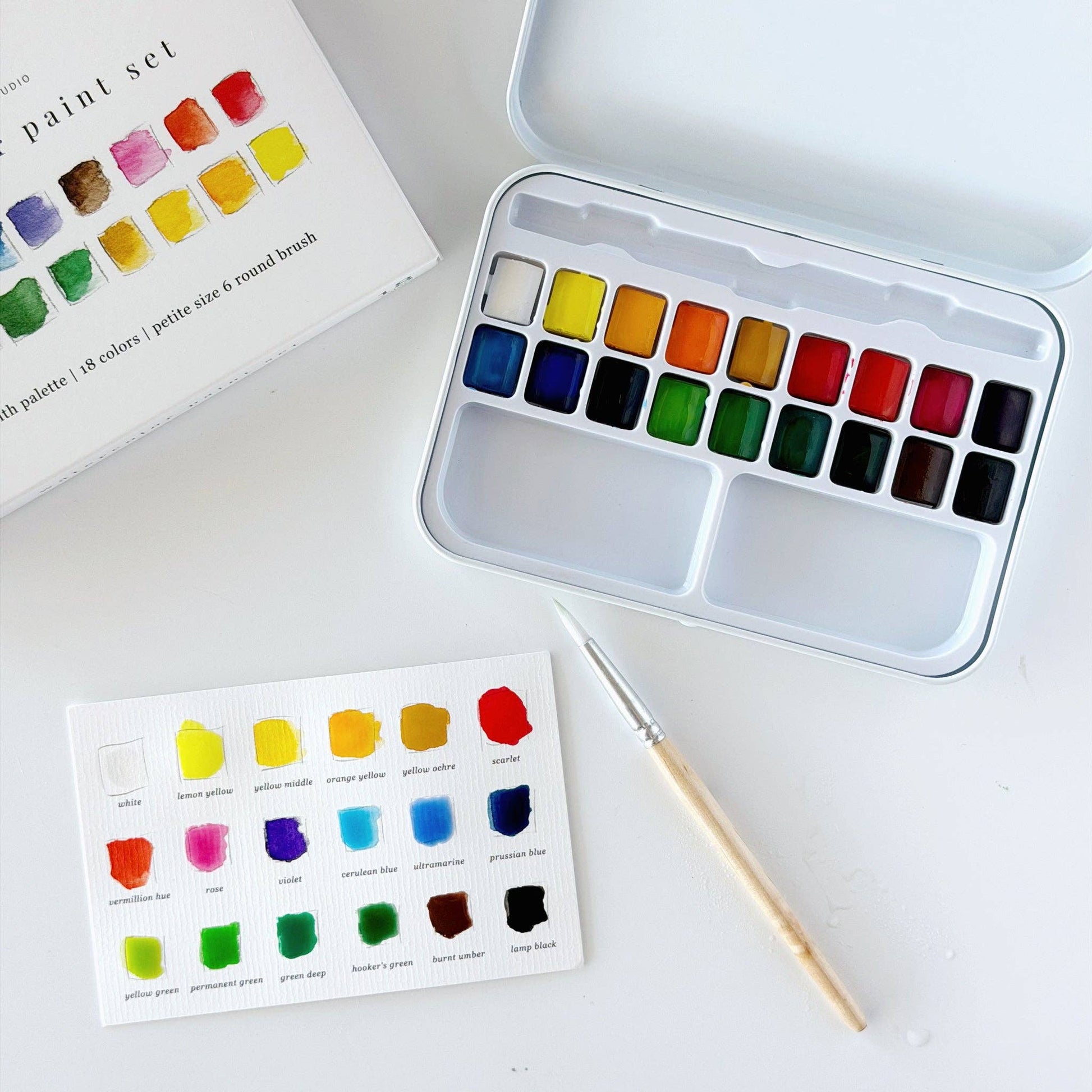 Portable watercolor paint set paired with an Emily Lex watercolor workbook on a wooden table, creating a peaceful space for creativity.