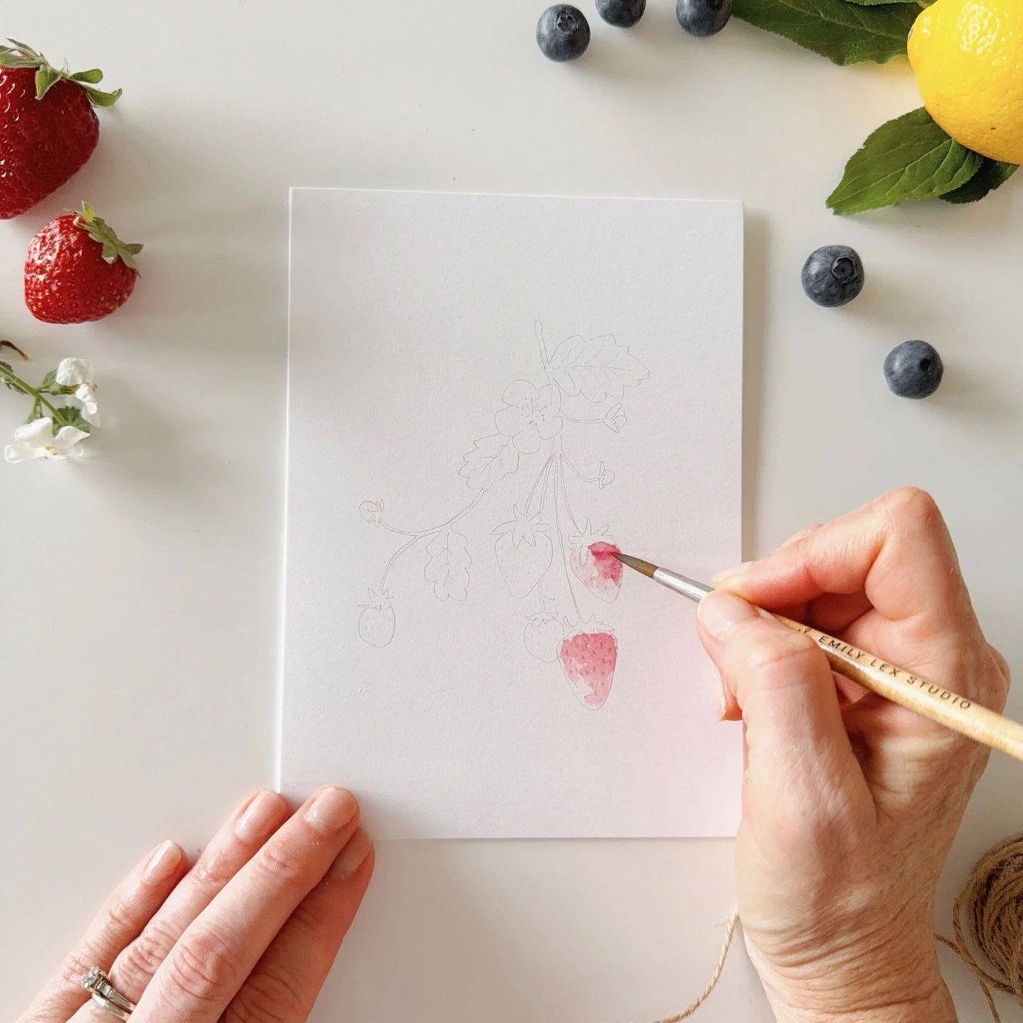 Close-up of the watercolor paper and illustrated fruit designs ready to be painted.