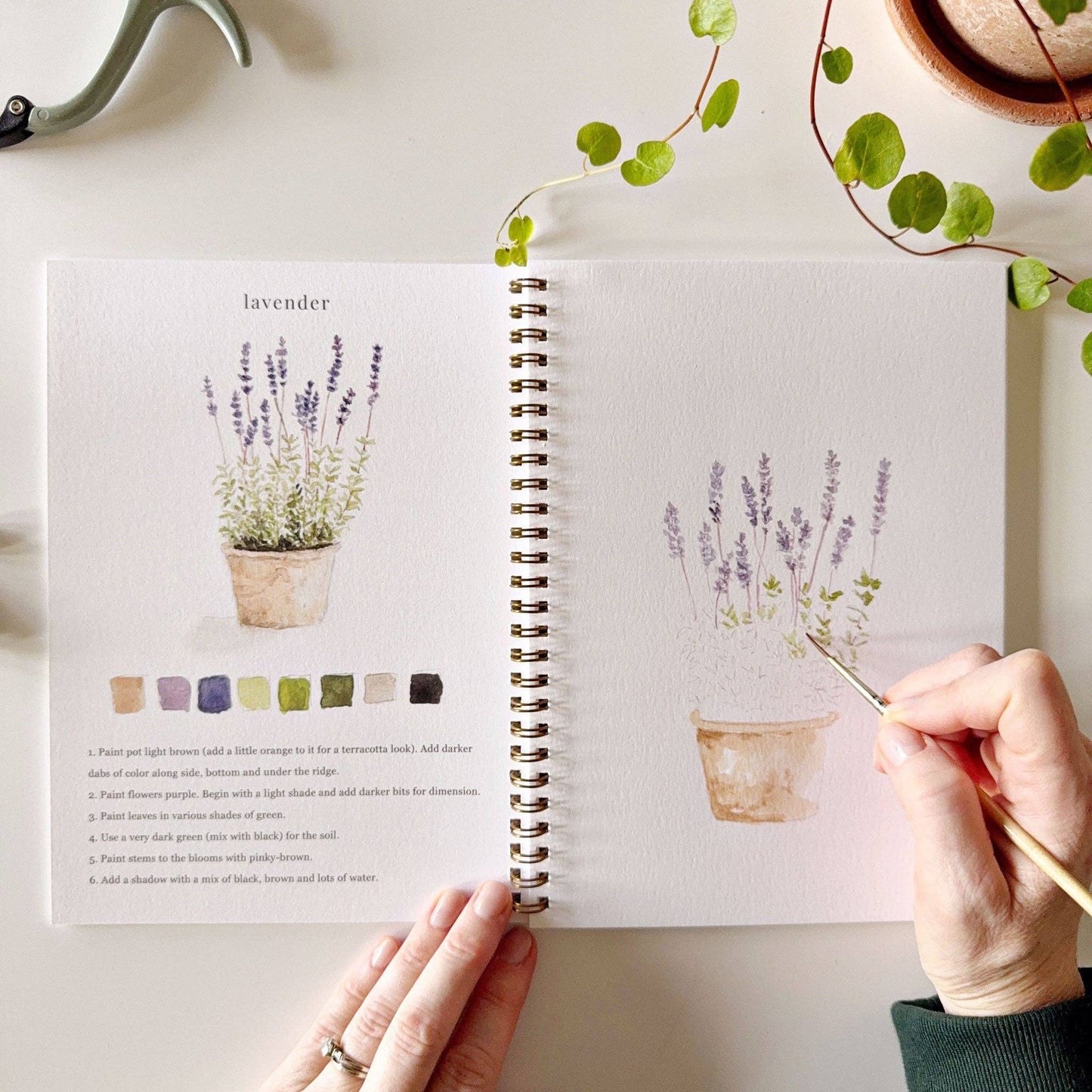 Botanical watercolor workbook styled with paints and brushes on an art table.