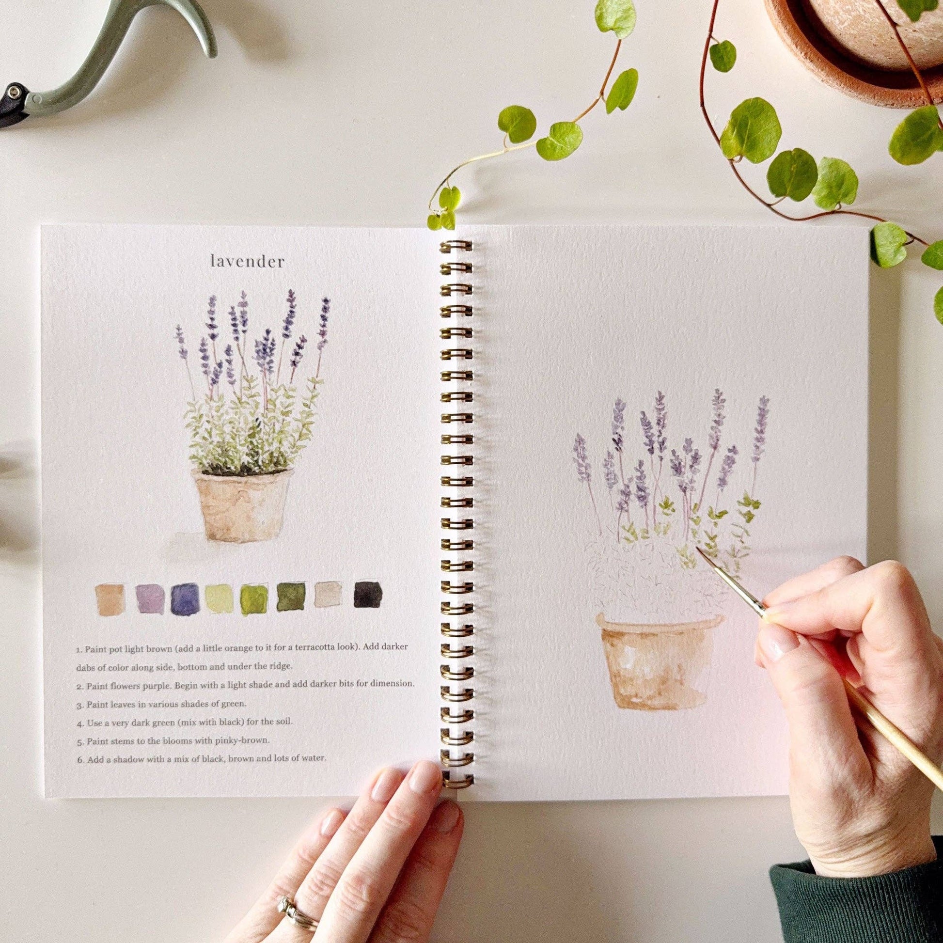Botanical watercolor workbook styled with paints and brushes on an art table.