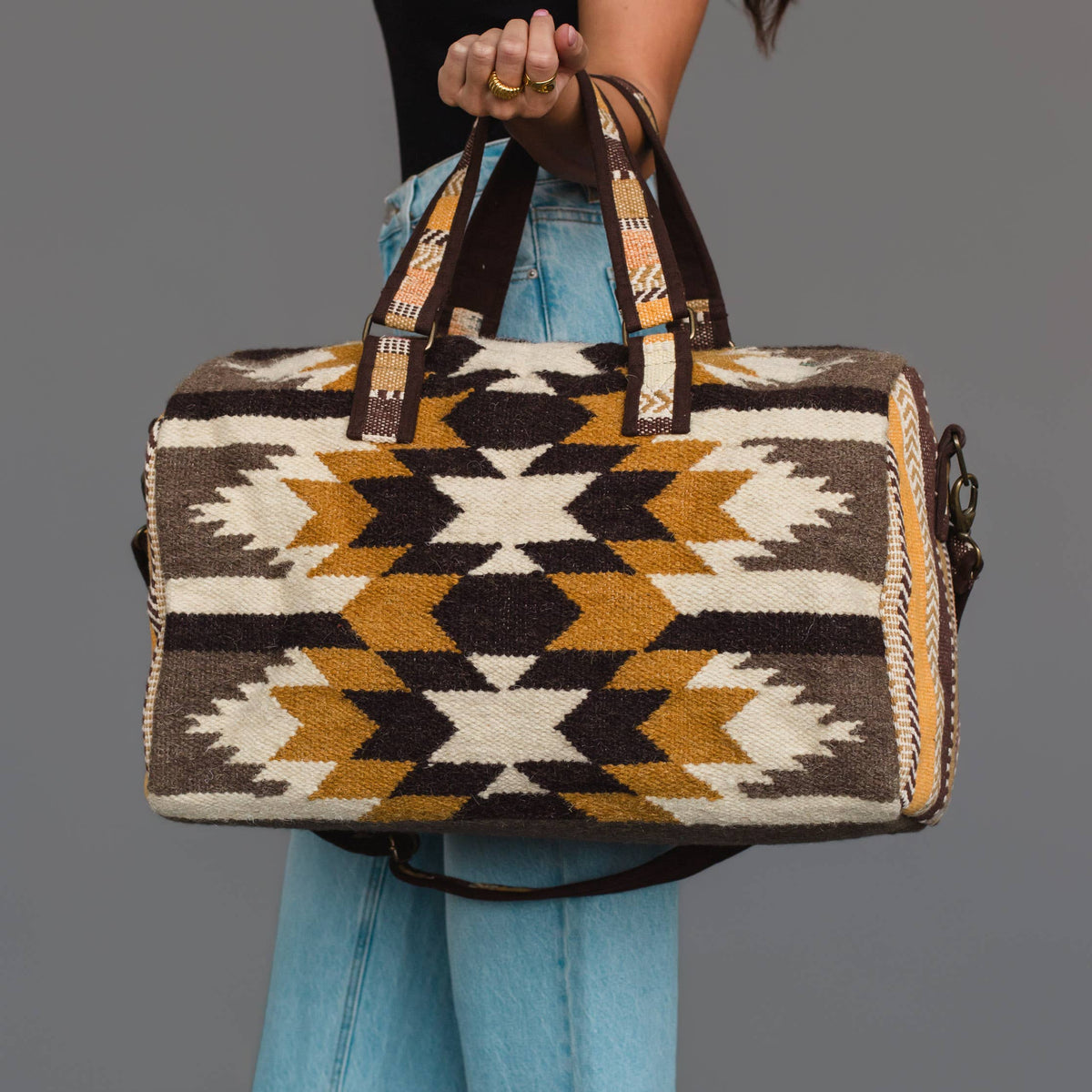 Western geometric cotton duffel bag in dark brown, camel, tan, and beige with sturdy top handles and an adjustable shoulder strap.