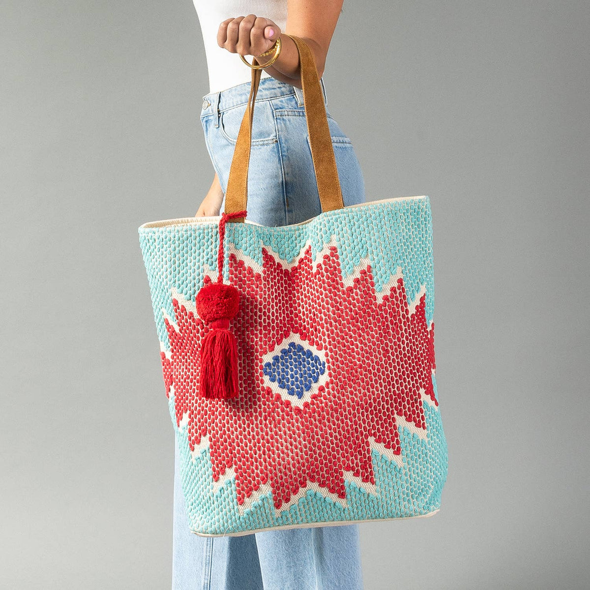Western geometric cotton tote bag in red, turquoise, and blue with suede leather shoulder straps and a coordinating red tassel.