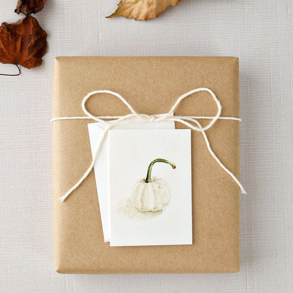 White pumpkin mini enclosure card tucked into a wrapped hostess gift with linen ribbon, leaves, and kraft paper.