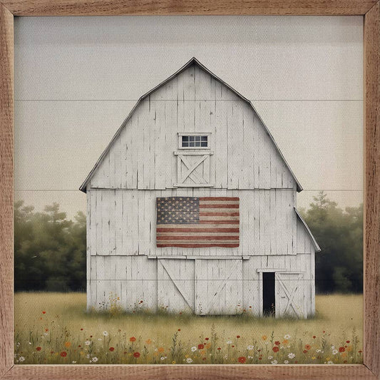 White barn with American flag on a grassy field, framed in wood.