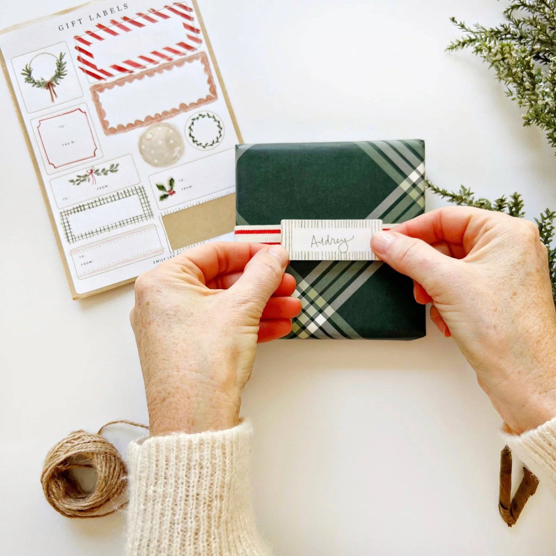 Christmas gift tag stickers applied to wrapped presents with ribbon, evergreen sprigs, and festive holiday décor.